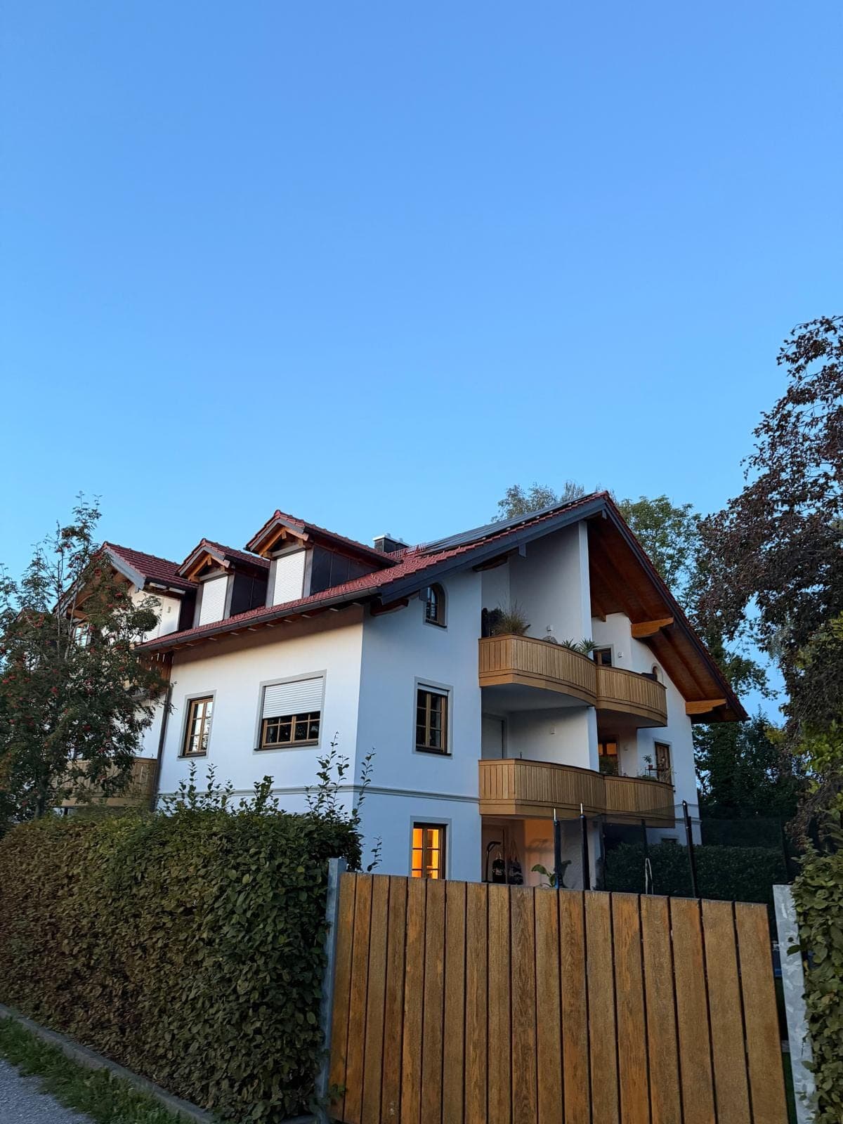 Mehrfamilienhaus mit Holzbalkonen hinter einem Holzzaun