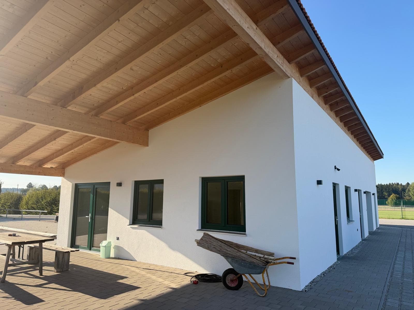 Weiß verputzter Flachbau mit grünen Fenstern und Holzdach